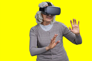 Old happy caucasian woman wearing virtual reality goggles. Senior lady playing on color background.