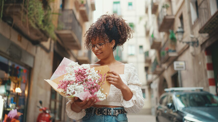 Young woman in glasses holding a bouquet of flowers on the street of the downtown. Girl with bouquet of flowers on the street on urban background