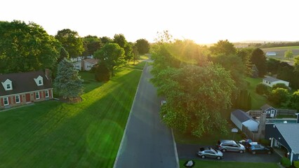 Beautiful sunset over quaint American neighborhood. Green trees grow leaves in spring. Small town housing in rural USA. - Powered by Adobe