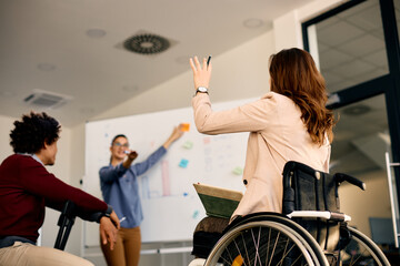 Rear view of businesswoman in wheelchair raising arm to ask a question during presentation in the office. - Powered by Adobe
