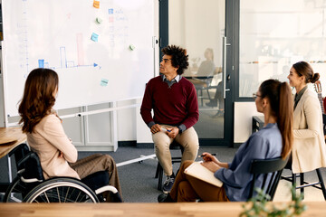 Black businessman explaining his coworkers business strategy on whiteboard during presentation in...