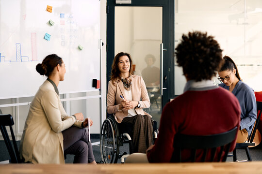 Happy disabled businesswoman brainstorming with her coworkers during presentation in meeting room.