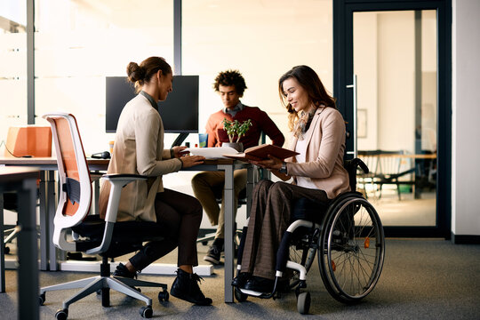 Happy businesswoman in wheelchair going through reports with her colleague in office.