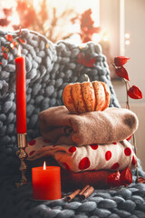 Obraz na płótnie Canvas Cozy autumn still life with stapled knitted wool sweaters, candle, pumpkin and branches at grey blanket. Warm clothes for cold days. Front view.