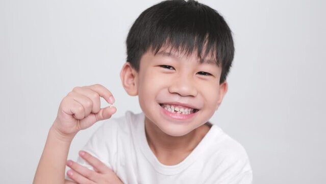 Asian kid holding the first fallen baby milk teeth while the second tooth loses and bends in his mouth. A happy boy proudly smiles at his dental care.