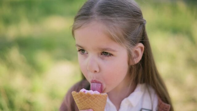 Little cute girl eating ice cream and looking at camera smiling. Close-up outdoor portrait.