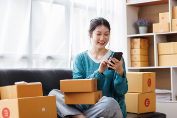 Fototapeta na wymiar Asian business woman on sofa using a laptop computer checking customer order online shipping boxes at home. Starting SME Small business entrepreneur freelance. Online business, SME Work home concept.