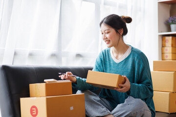 Asian business woman on sofa using a laptop computer checking customer order online shipping boxes at home. Starting SME Small business entrepreneur freelance. Online business, SME Work home concept.