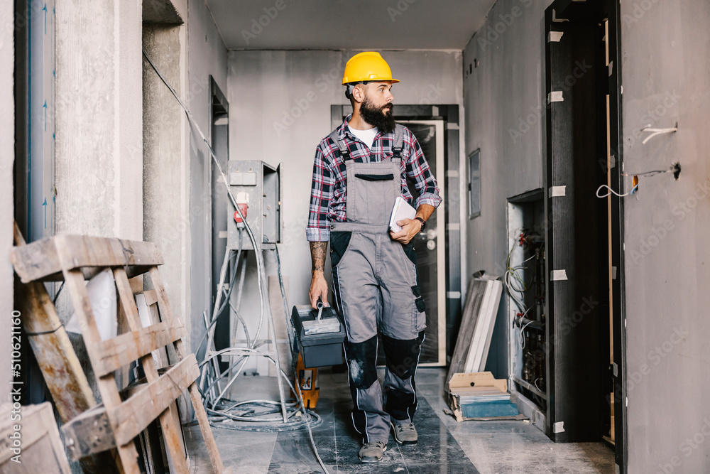 Wall mural a worker with toolbox arrives at his workplace, unfinished building.