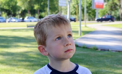 The blond boy looks up in surprise. A bewildered five-year-old boy against a blurry green background. 