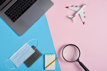 Pandemia travel by air. Search concept. Top view of a laptop with aeroplane, passport and medicine mask over doutone blue and pink background
