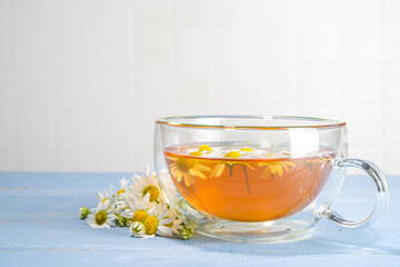 Cup of brewed chamomile tea with  bouquet of chamomile daisy, blue wooden background copy space. Herbal organic cold drink.