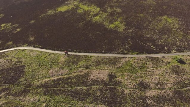 Aerial drone shot of car driving along scenic road through green countryside in Exmoor National Park, UK