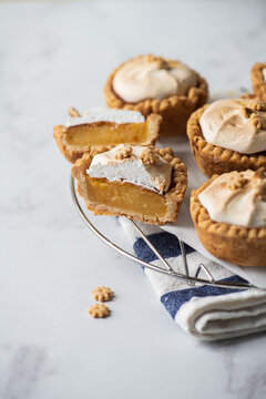 Lemon curd tartlets with whipped meringue on a wire rack on a gray background.
