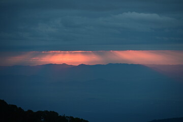 The orange sun shines through the clouds down the mountain in the morning. The beautiful scenery of the sunrise over the mountains on a winter morning.

