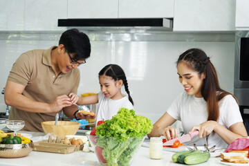 family of parents and their six-year-old daughter cook bread and sandwiches for breakfast at home.