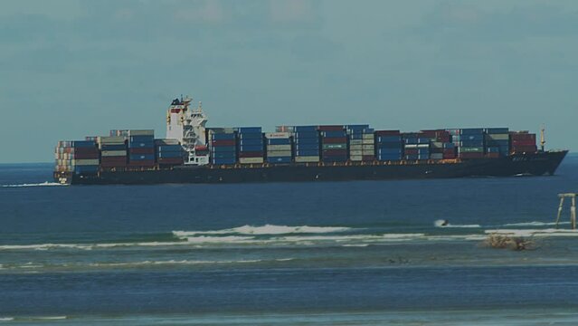 A jet ski rider jumps a wave as a large fully loaded containership steams past.