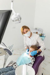 Beautiful kid boy smiling in dentist's chair the office treats teeth. Doctor mask and child looks at camera.