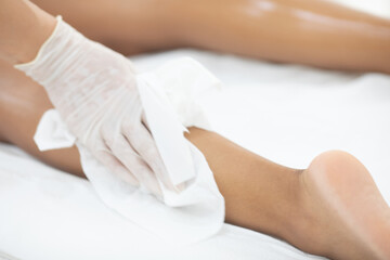 Obraz na płótnie Canvas The cosmetologist in medical gloves removes agent gel from the client's legs. The concept of hair removal in a professional beauty salon.