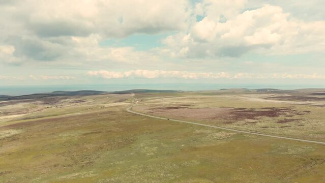 Aerial drone shot of car driving along scenic road through green countryside in Exmoor National Park, UK