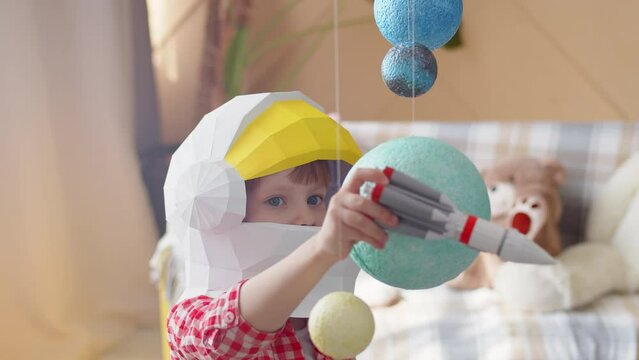 Caucasian child in a space helmet plays with a rocket and artificial planets, the concept of the future. Young boy dreams of cosmonautics