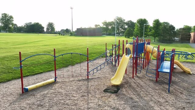 Low aerial orbit of large playground at American elementary school. Early morning sun on summer day reflects off metal fixtures.