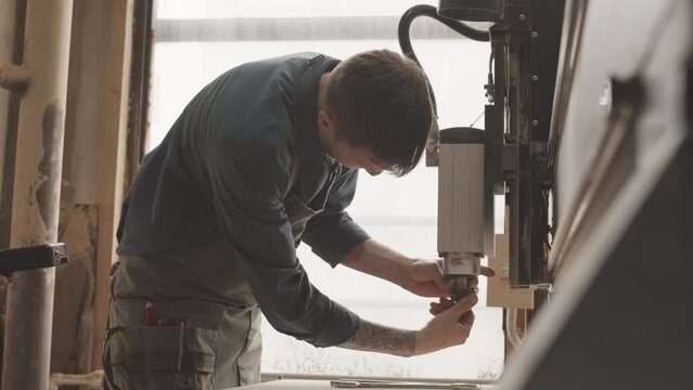Caucasian male carpenter using wrench while repairing CNC machine in woodworking workshop