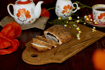 Traditional poppy seed buns, cup of black tea and milk among poppies flowers and dishes with poppies ornaments. Delicious breakfast. Summer lifestyle countryside photography.