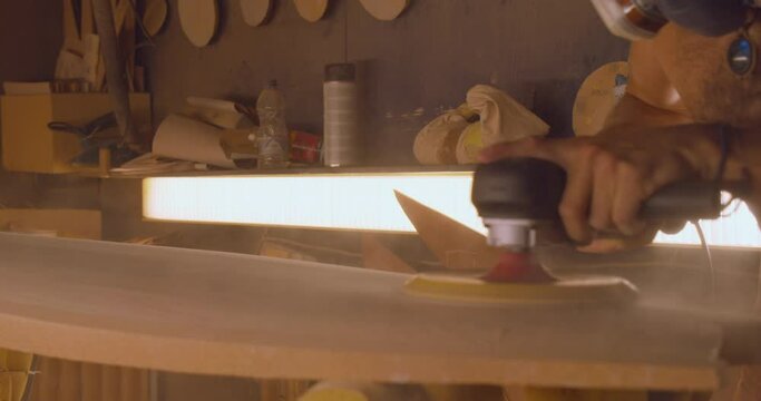 Masculine artisan man wearing jewelry working with a sanding machine on a piece of wood