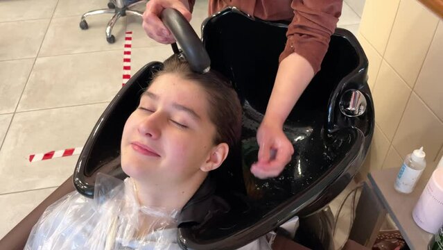 a girl - a hairdresser washes a girl of 13 years old head in a beauty salon, taking care of a shower in a beauty salon