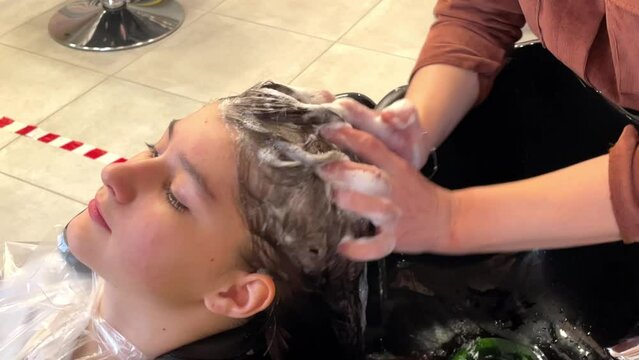 a girl - a hairdresser washes a girl of 13 years old head in a beauty salon, taking care of a shower in a beauty salon