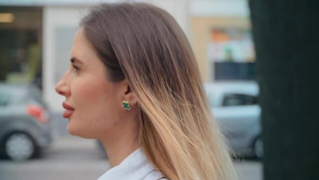 Portrait young sunshine woman with blonde hair walking in European city street. Modern urban town landscape, female wearing spring clothes