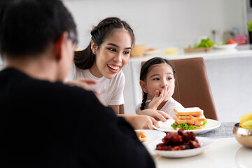 Asian girl eating at the dinner table with mom and dad inside the house happy family