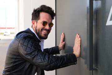 handsome young man with beard, sculpted body and sunglasses is leaning with both hands on the grey door of his garage looking at the camera for the portrait. Concept different expressions.