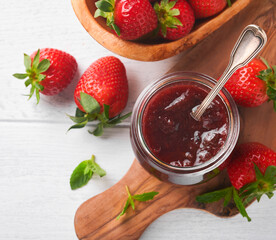 Strawberry jam. Strawberry jam in glass jar with fresh berries plate on white wooden table background, closeup. Homemade strawberry fruity jam. Top view with copy space.
