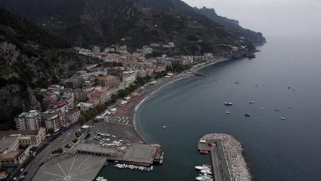 Drone video of a discovery plane passing a palace and revealing the city of Maiori on the Amalfi Coast, Italy. In the scene you can see boats, vehicles in traffic time.