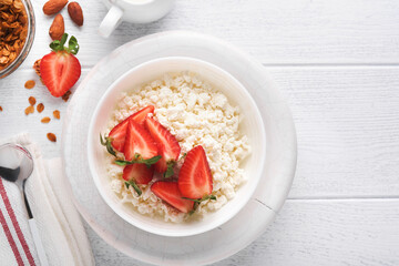 Cottage cheese with strawberries. Breakfast from cottage cheese with slices fresh strawberries, cream, cup of coffee in white bowl on white wooden background. Top view. Food concept. Mock up.