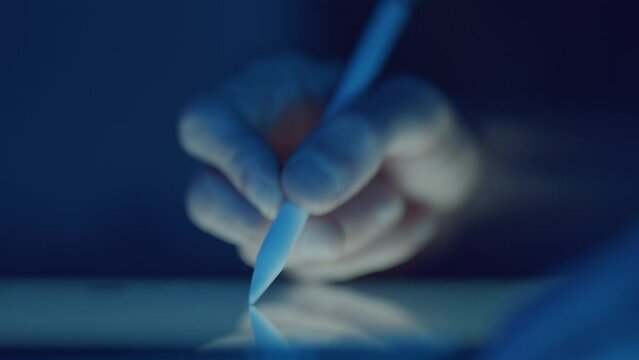 Designer sketching with digital stylus on glowing graphics tablet at night