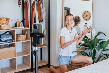 Young woman blogs about houseplants. girl in casual clothes takes care of plants at home and makes a video of her smartphone in her apartment.