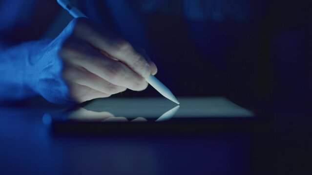 Designer sketching with digital stylus on glowing graphics tablet at night