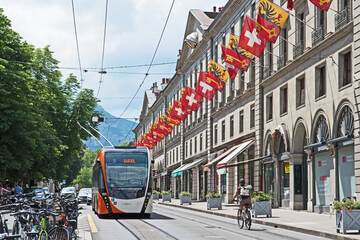 A trolly bus passes through the rue de la Corraterie whose buildings are decked with the flags of...