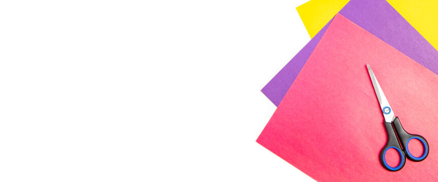 Scissors lie on colored paper on a white background. Top view, flat lay. Banner