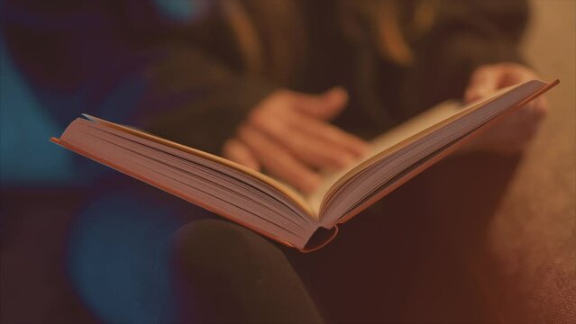 Close up of a young woman reading a hardback book on a cosy couch