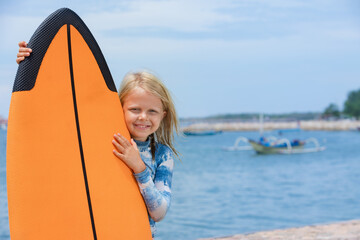 Happy baby girl - young surfer learn to ride on surfboard with fun on sea waves. Active family...