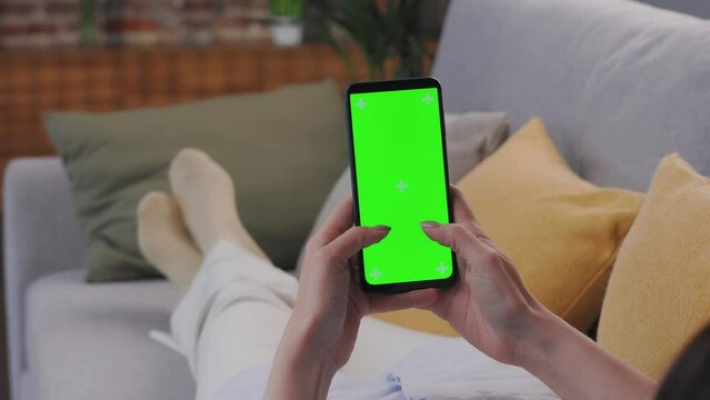 Close up view of female hands using smartphone with green mock-up screen. Scrolling through social media or online shop, swiping photos or pictures, surfing Internet,watching content videos blogs.