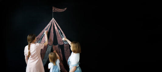 Three children draw circus tent on black chalk board, concept of children's creativity and imagination, copy space