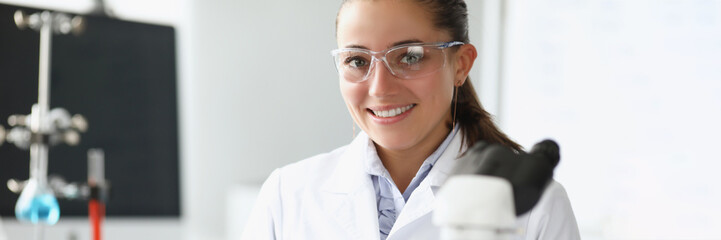 Pretty cheerful laboratory worker in medical gown examine sample under microscope