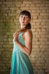 Portrait of a young beautiful dark-haired girl in a dress against a brick wall. There is artistic blur.