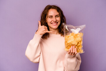 Young caucasian woman holding a bag of chips isolated on purple background showing a mobile phone call gesture with fingers.