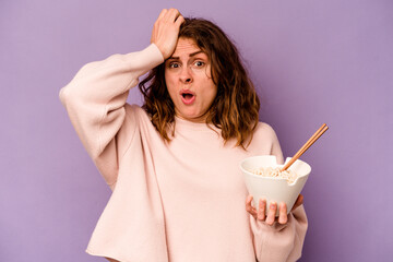 Young caucasian woman eating noodles isolated on purple background being shocked, she has...